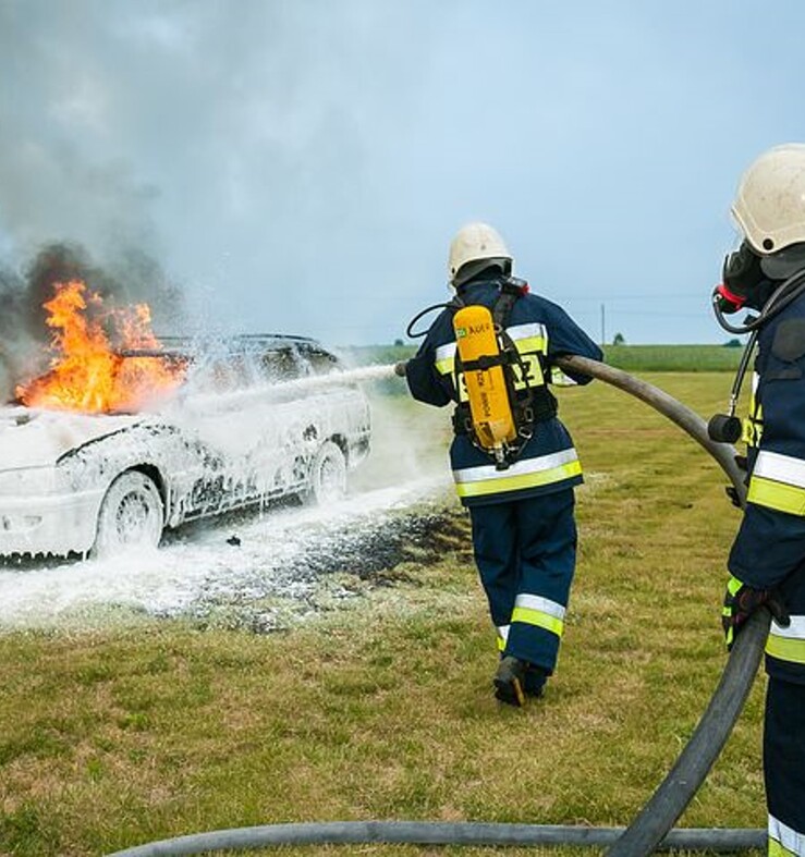 Afbeelding van een brandweerman die een auto blust met schuim.